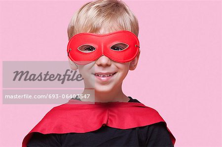 Portrait d'un garçon heureux en costume de super héros sur fond rose