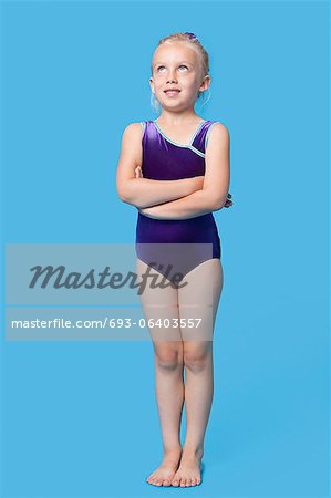 Young female gymnast with arms crossed looking up over blue background