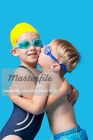 Jungen Geschwistern in Bademode, umarmen und küssen auf blauem Hintergrund