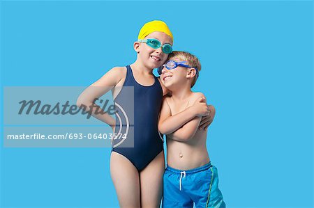 Happy young siblings in swimwear with arm around over blue background