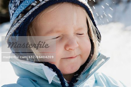 Toddler girl wearing winter clothes in snow with eyes closed, portrait