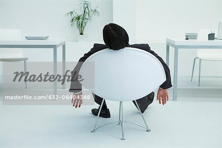 Businessman napping in chair in office, rear view