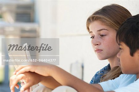 Children sitting together outdoors, looking at book