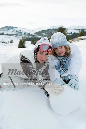 Teenage girls rolling snowball together, portrait