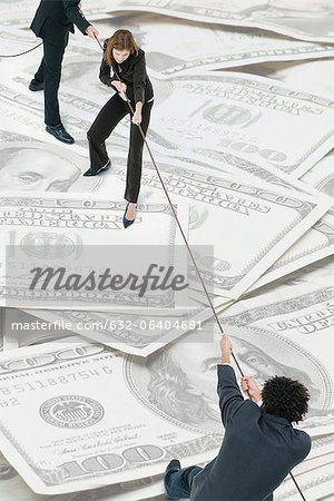 Executives playing tug-of-war on top of pile of one-hundred dollar bills