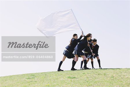 Japanese schoolgirls holding a white flag on the top of a hill in their uniforms