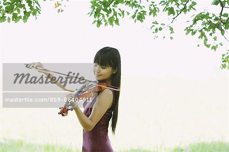 Asiatische Frau dem Geigenspiel auf einem Rasen