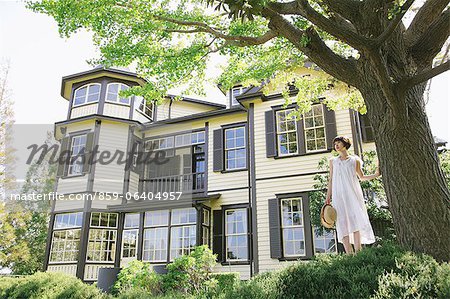 Femme japonaise en une robe blanche et due forme près d'un grand arbre avec une maison blanche dans le fond