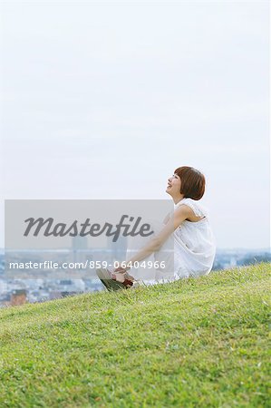 Japanische Frau mit kurzen Haaren in einem weißen Kleid auf dem Rasen sitzend