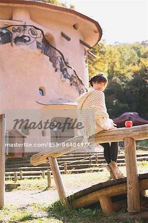 Japanese woman in a white cardigan sitting on a wooden rail and looking at camera