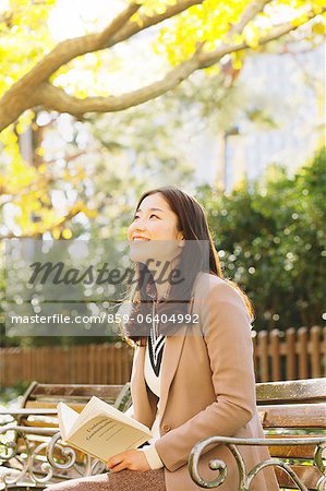 Femme japonaise avec des cheveux longs, assis sur un banc dans un parc, tenant un livre