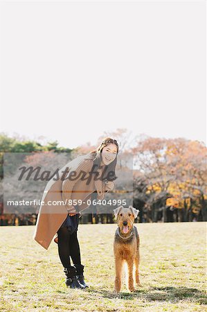 Femme japonaise avec longs cheveux et un chien dans un parc en regardant la caméra