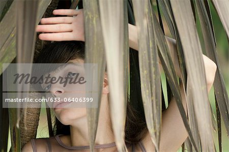 Jeune femme derrière les feuillages tropicaux, portrait