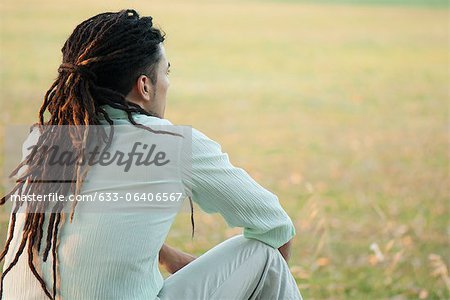 Homme avec des dreadlocks assis en plein air, vue arrière
