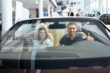 Jeune couple dans un cabriolet dans la salle d'exposition