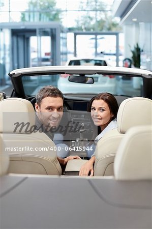 Jeune couple dans un cabriolet dans la salle d'exposition