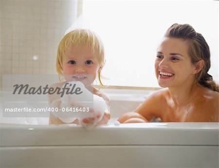 Bébé jouer avec de la mousse lors de la prise de bain avec la mère