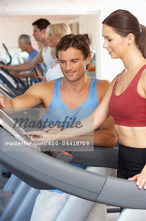 Frau, die zur Ausführung der Maschine im Fitnessstudio mit Personal Trainer arbeiten