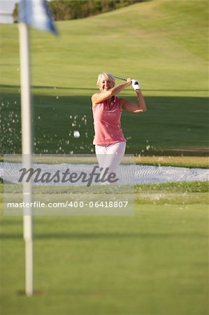 Senior Female Golfer Playing Bunker Shot On Golf Course