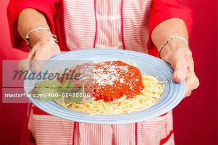 Gros plan des mains de mère tenant un plat de spaghetti maison marinara.
