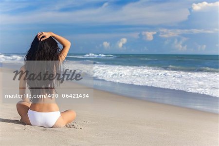 Une sexy jeune brunette femme ou une fille portant un bikini blanc, assis sur une plage tropicale déserte avec un ciel bleu