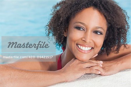 A beautiful sexy young African American girl or young woman wearing a bikini and relaxing on the side of a swimming pool.