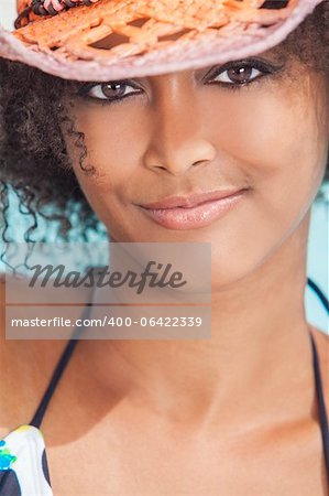 A beautiful sexy young African American girl or young woman wearing a bikini and straw cowboy hat with swimming pool in the background