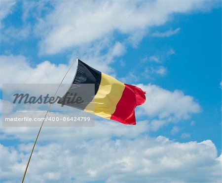 belgian flag in a strong breeze against a blue cloudy sky