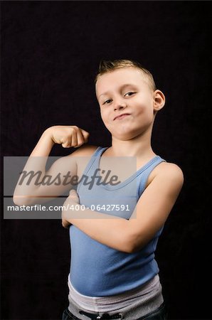 A young boy showing off his muscles on black background