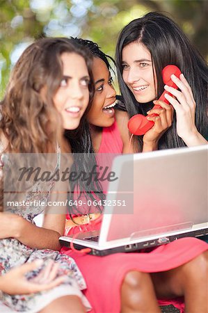 Frauen mit Laptop und Handy, während auf einem Ast sitzend