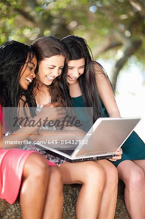 Women using laptop whilst sitting on a tree branch