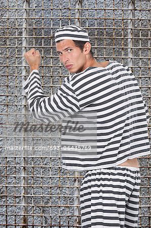 Portrait de jeune homme prisonnier en uniforme debout contre une cellule de prison