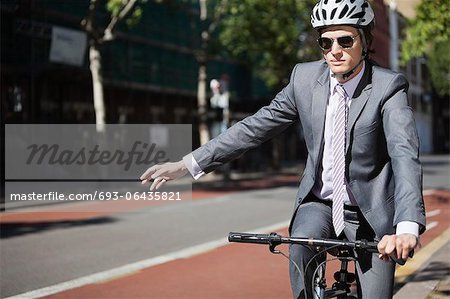 Junger Geschäftsmann mit Handzeichen beim Fahrradfahren Junger Geschäftsmann mit Handzeichen beim Fahrradfahren