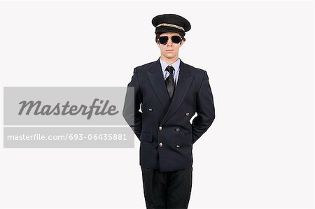 Young man in pilot uniform standing against gray background