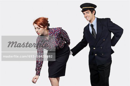 Portrait of young pilot touching flight attendant inappropriately against gray background