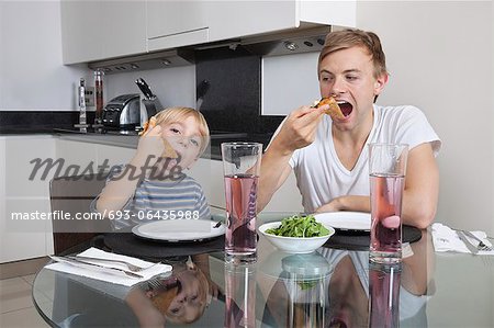 Father and son eating pizza at breakfast table