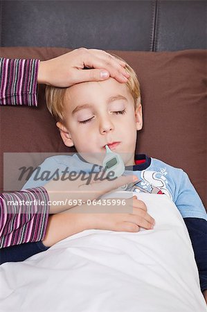Mother checking unwell little boy's temperature with thermometer