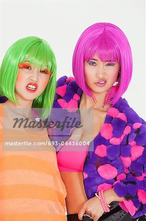 Portrait of two female friends wearing wigs against gray background