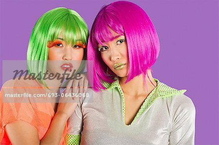 Portrait of two female friends wearing wigs against gray background