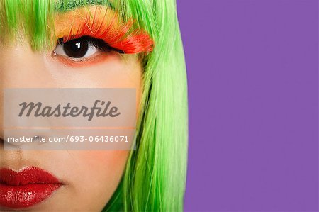 Cropped image of young woman wearing false eyelashes against purple background