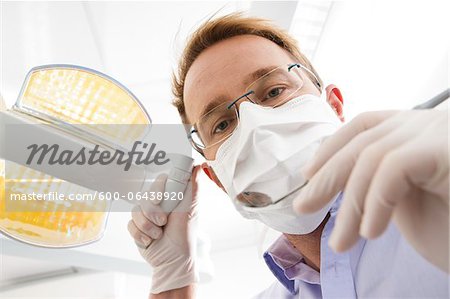 Dentist wearing Surgical Mask Adjusting Light and looking down, Germany