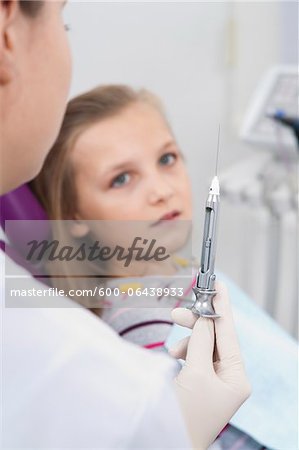 Girl Looking at Needle held by Dentist, Germany