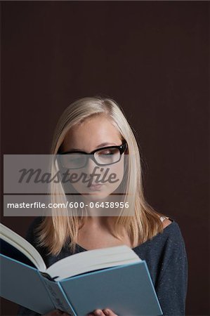 Portrait of Blond, Teenage Girl wearing Eyeglasses and Reading Book, Studio Shot on Black Background