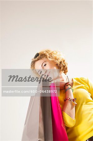Low Angle View Portrait of Blond Teenage Girl with Curly Hair, holding Shopping Bags and Smiling at Camera, Studio Shot on White Background