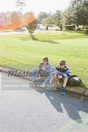 Two Boys Sitting on Neighbourhood Curb with Handheld Electronics