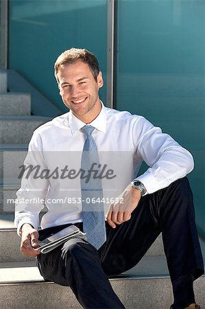 Smiling businessman sitting with tablet PC and newspaper on stairs