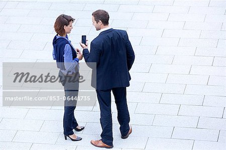 Businessman and businesswoman standing with cell phone outdoors