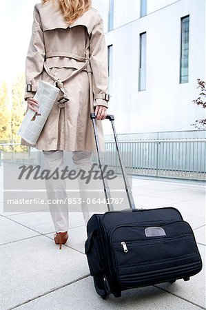 Businesswoman with trolley suitcase on pavement