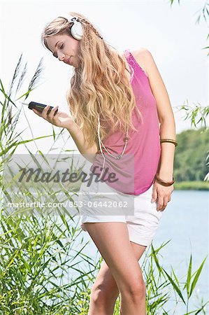 Blonde jeune femme à l'écoute de la musique à un lac