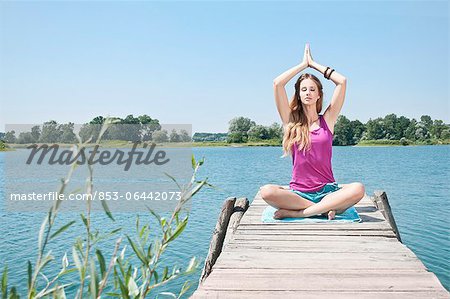 Blond young woman practicing yoga at a lake